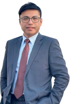 A man in a suit and tie stands with one hand in his pocket, looking forward.