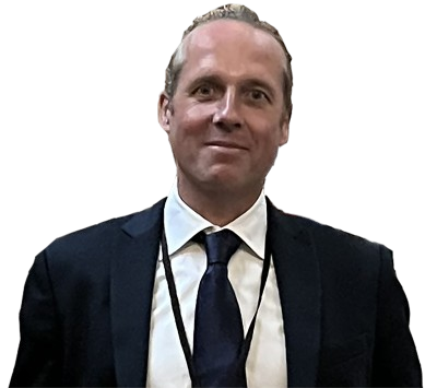 A man in a suit and tie with a lanyard around his neck, standing against a plain background.