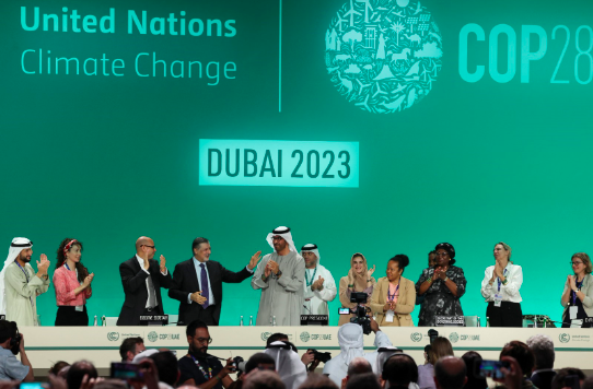 A group of people on stage at the United Nations Climate Change event, COP28, with a green backdrop reading "DUBAI 2023.