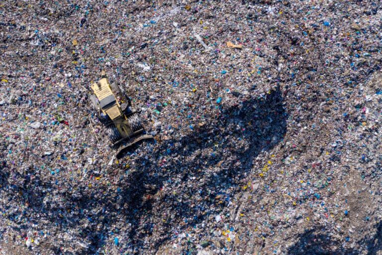 Aerial view of a bulldozer moving garbage in a large landfill, surrounded by piles of waste.