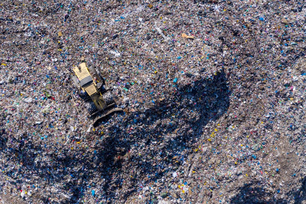 Aerial view of a bulldozer moving garbage in a large landfill, surrounded by piles of waste.