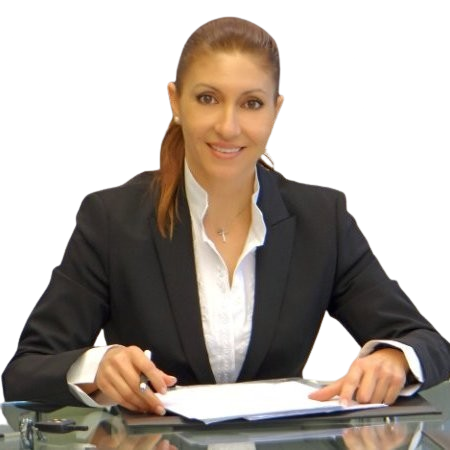 A person in a business suit sits at a table with documents, smiling and holding a pen.