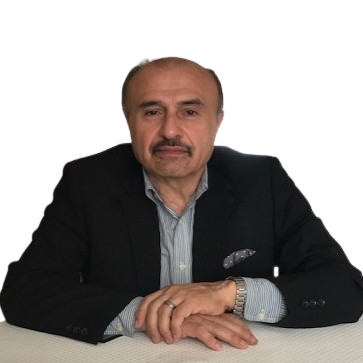 A man in a black suit and blue shirt sits at a table with his hands folded.