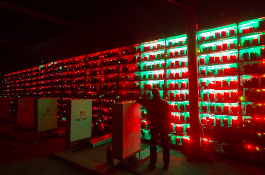 A person stands in front of illuminated servers with red and green lights in a dark room.