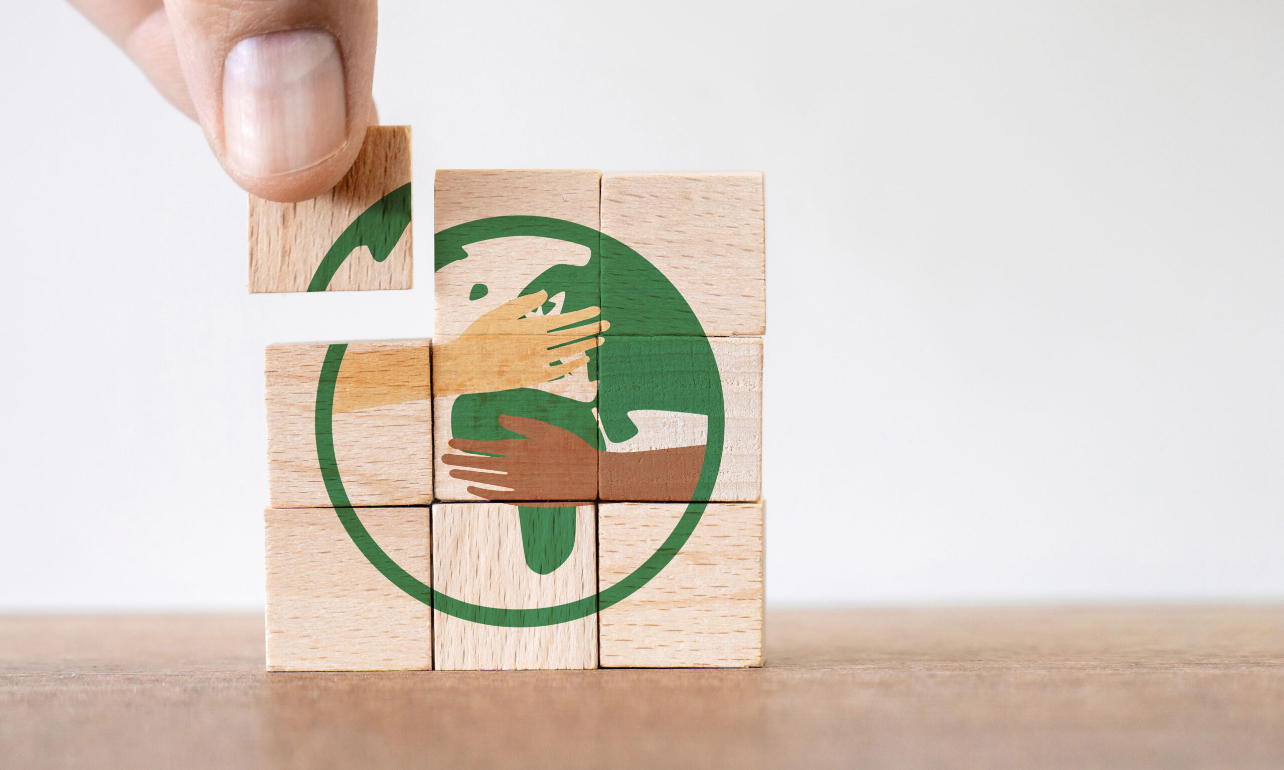 A hand places a wooden block to complete a puzzle showing hands of different skin tones embracing the Earth, symbolizing unity and environmental care.
