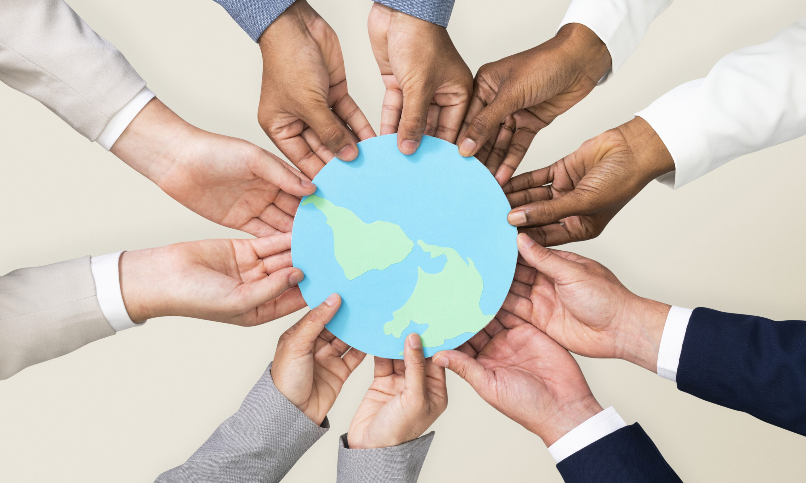 A group of diverse hands are holding a paper cutout of Earth, symbolizing unity and global cooperation.