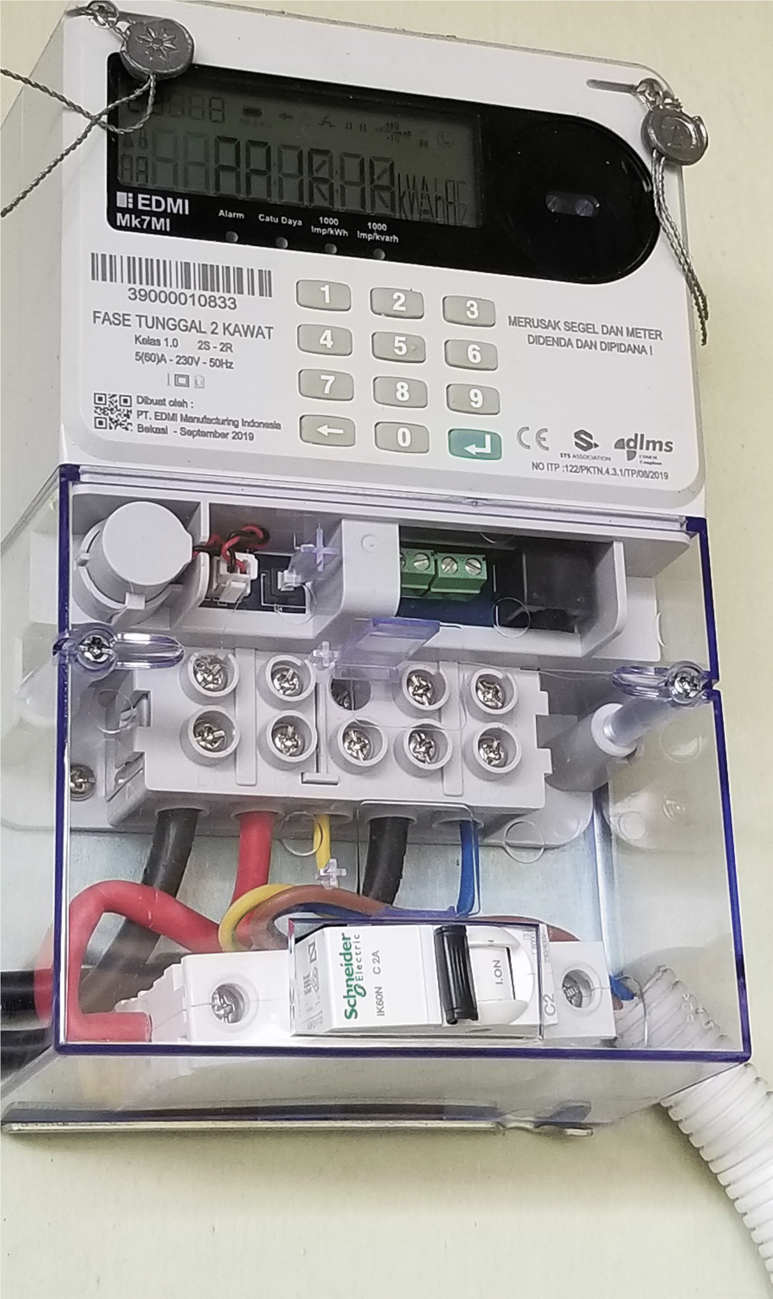 Close-up of an electric meter with visible wiring and a circuit breaker inside a transparent protective box mounted on a wall.